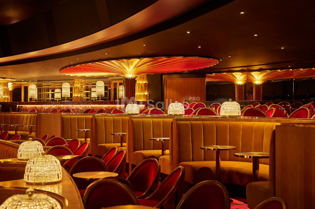 Salle de restaurant élégante avec banquettes en velours, chaises rouges et éclairage chaleureux sous un plafond décoratif.