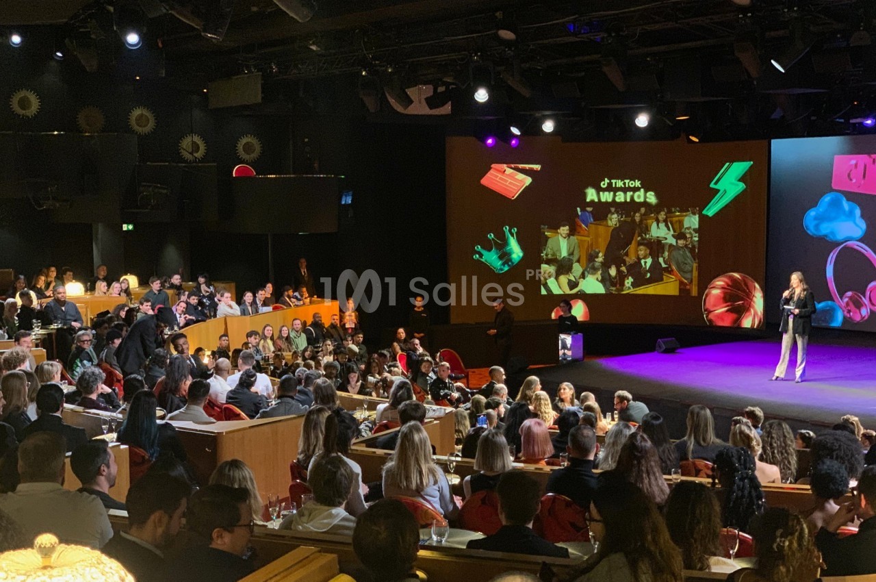 Salle comble lors d'une cérémonie de remise de prix, avec une scène éclairée et un public attentif.