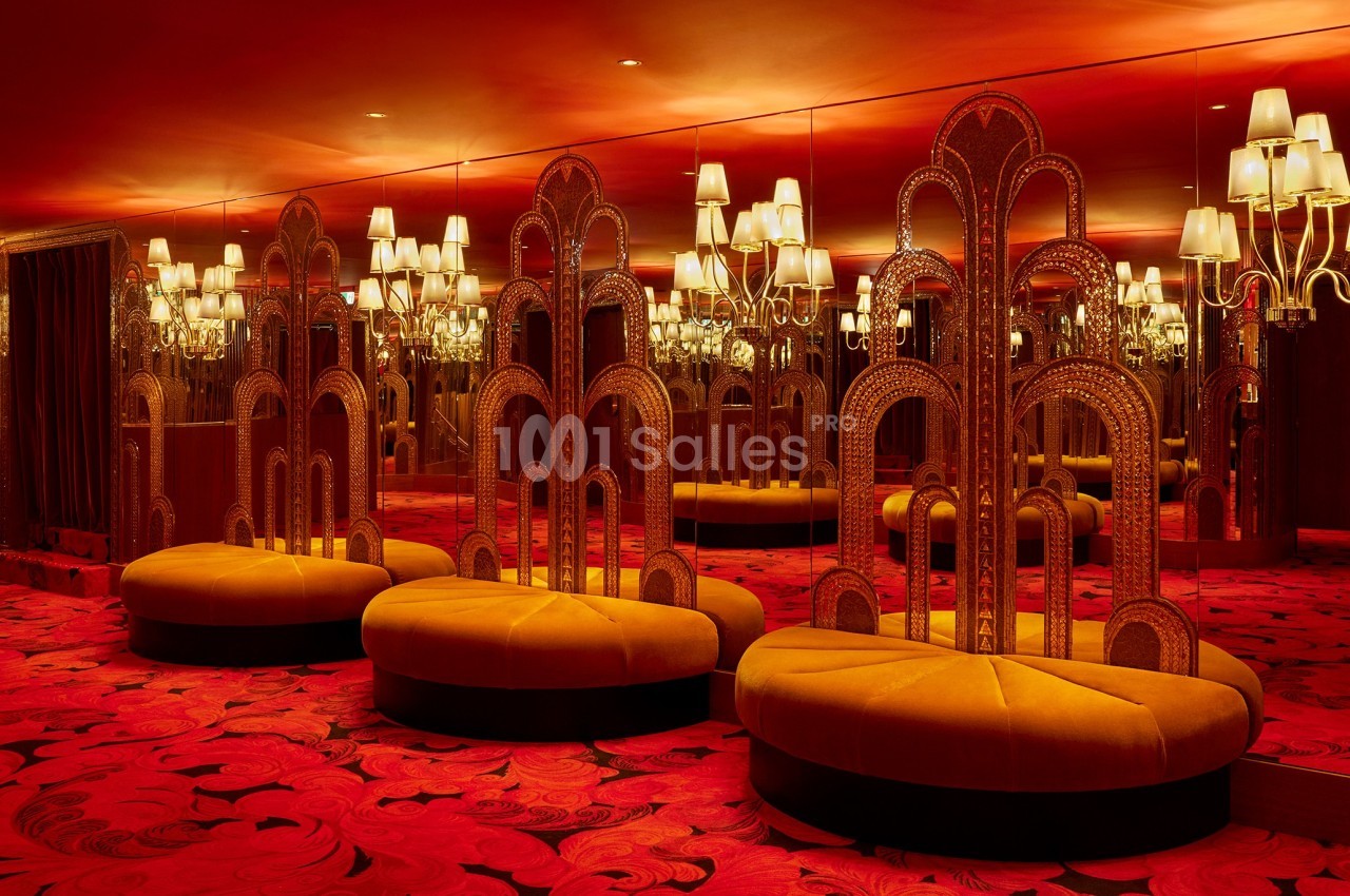 Banquettes jaunes et miroirs entourés de lampes dans une pièce au décor rouge avec motifs au sol.