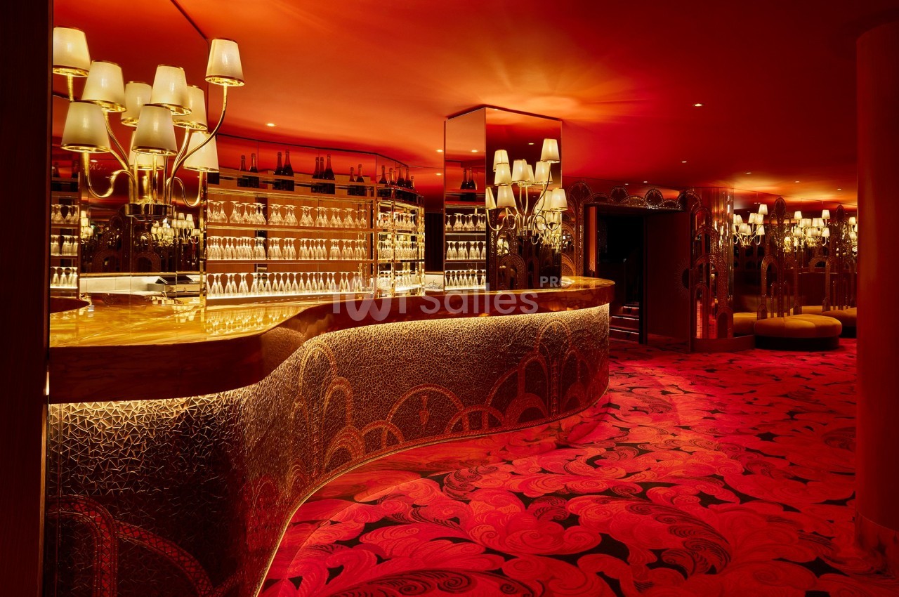 Bar luxueux avec comptoir doré, éclairage tamisé, murs et sol rouges ornés de motifs décoratifs.