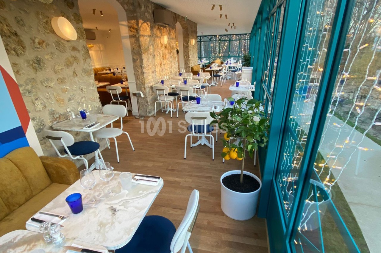 Salle de restaurant lumineuse avec des tables en marbre, des chaises blanches et de grandes baies vitrées donnant sur l…