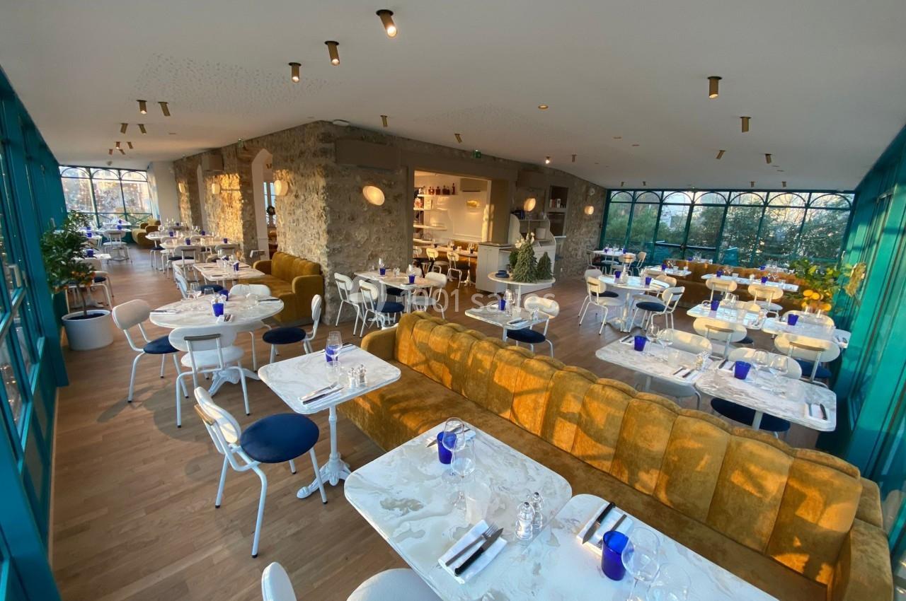 Salle de restaurant lumineuse avec grandes baies vitrées, mobilier moderne et tables dressées.