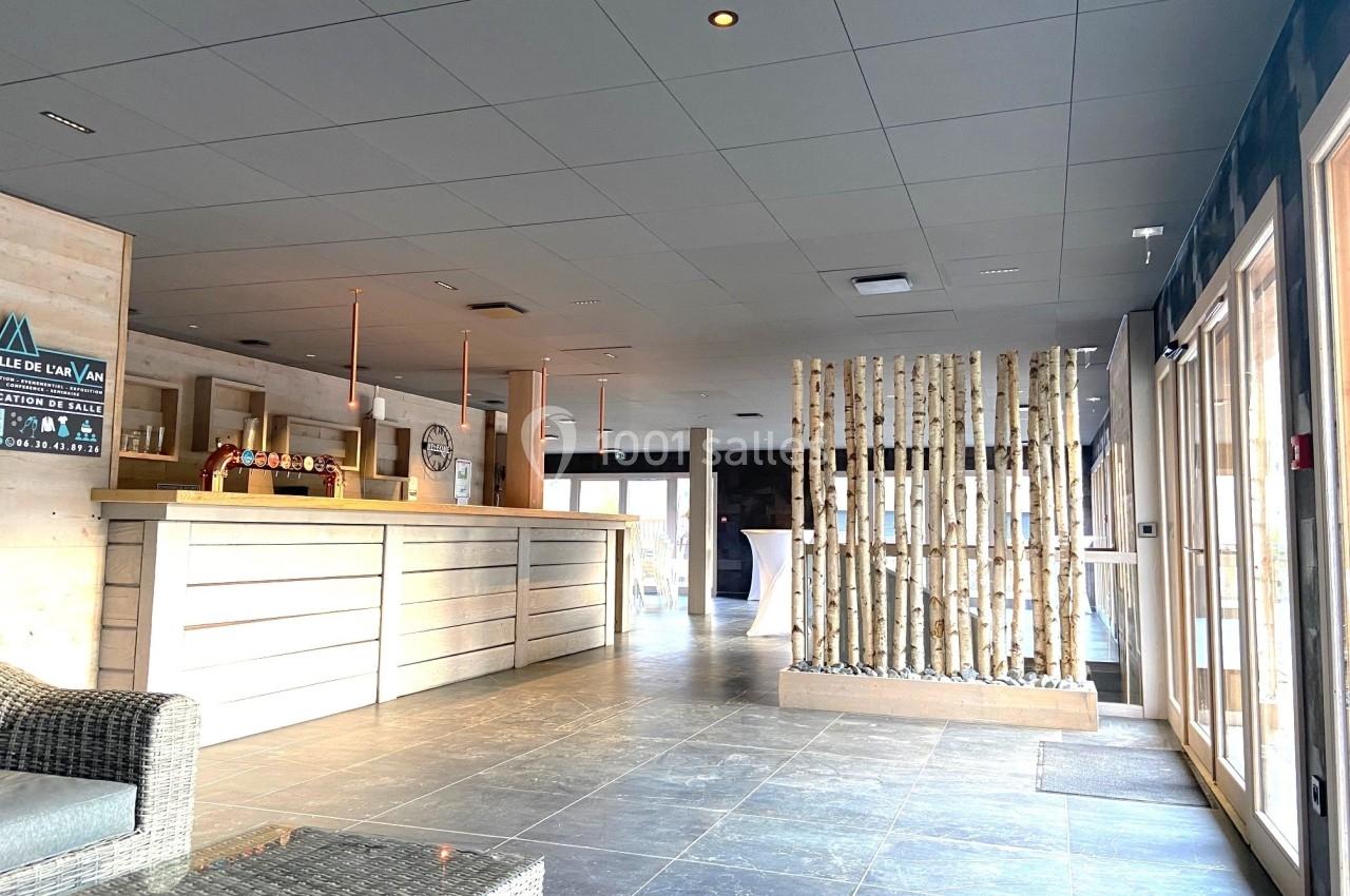 Hall d'accueil lumineux avec comptoir en bois clair, sol en carrelage gris et séparation en troncs d'arbres.