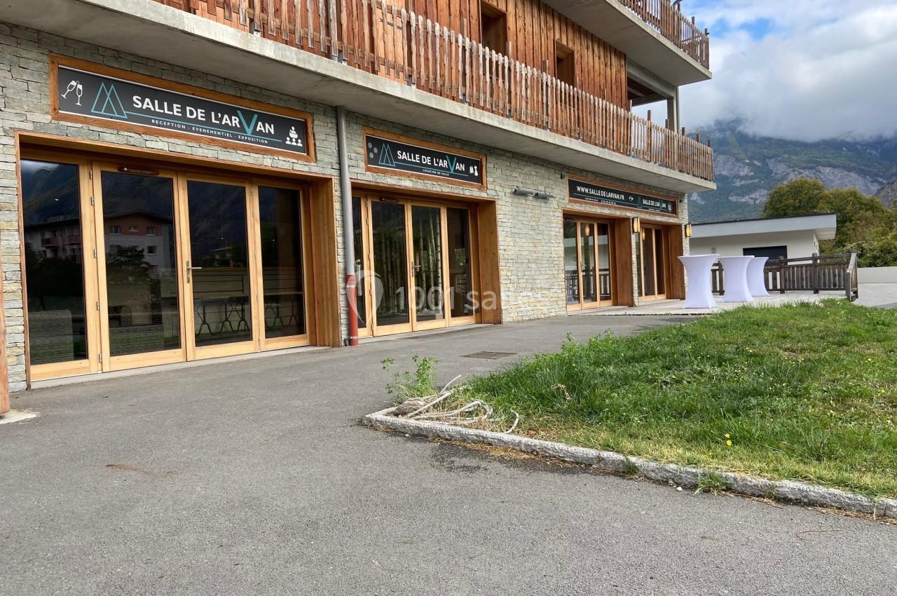 Façade d'un bâtiment en bois et pierre avec des baies vitrées et des enseignes indiquant ’Salle de l'Arvan’.
