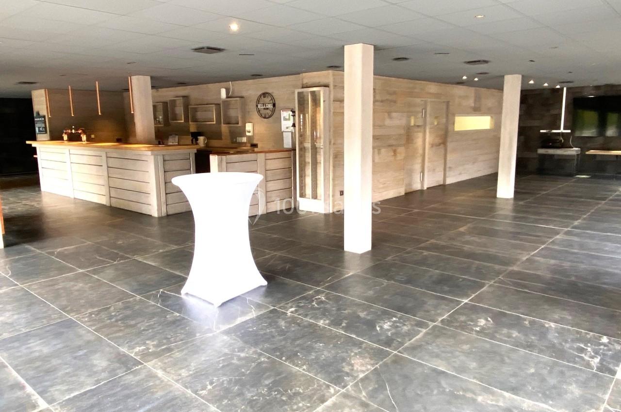 Salle spacieuse avec sol en carrelage sombre, comptoir en bois clair et table haute recouverte d'une nappe blanche.