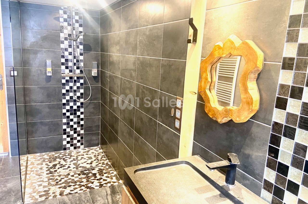 Salle de bain moderne avec douche à l'italienne, carrelage noir et blanc, miroir en bois sculpté et lavabo noir.
