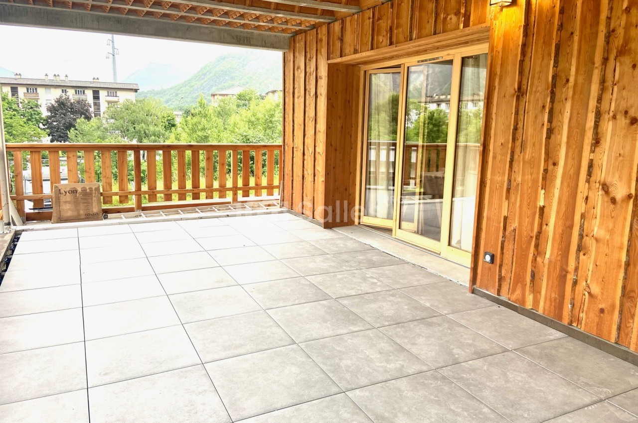 Terrasse spacieuse avec sol carrelé, balustrade en bois et vue sur des arbres et des collines verdoyantes.