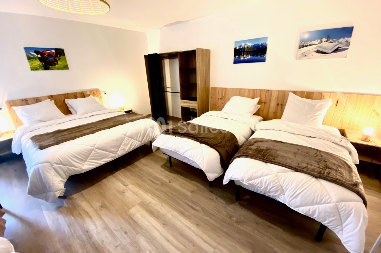 Chambre lumineuse avec deux lits simples et un lit double, parquet au sol, décorations murales et éclairage chaleureux.