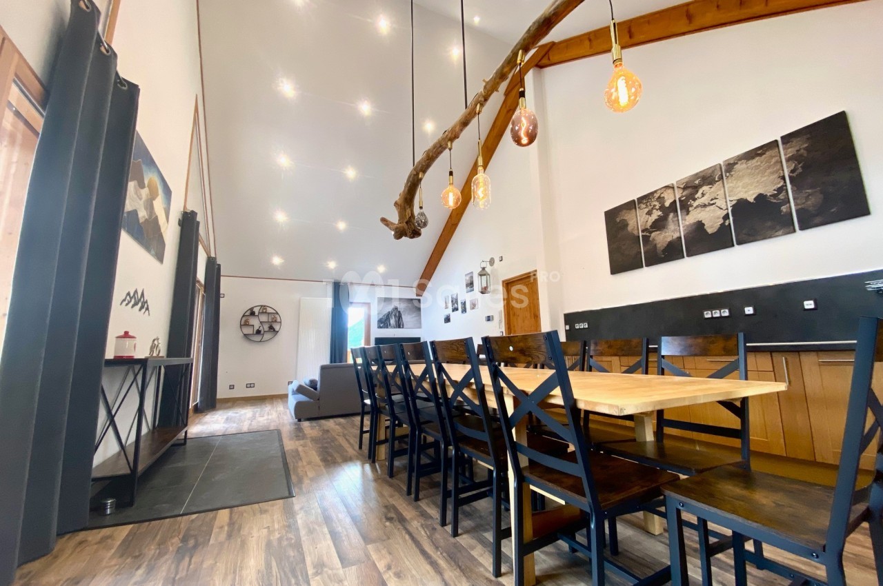 Salle à manger spacieuse avec table en bois, chaises noires, éclairage suspendu et plafond haut.