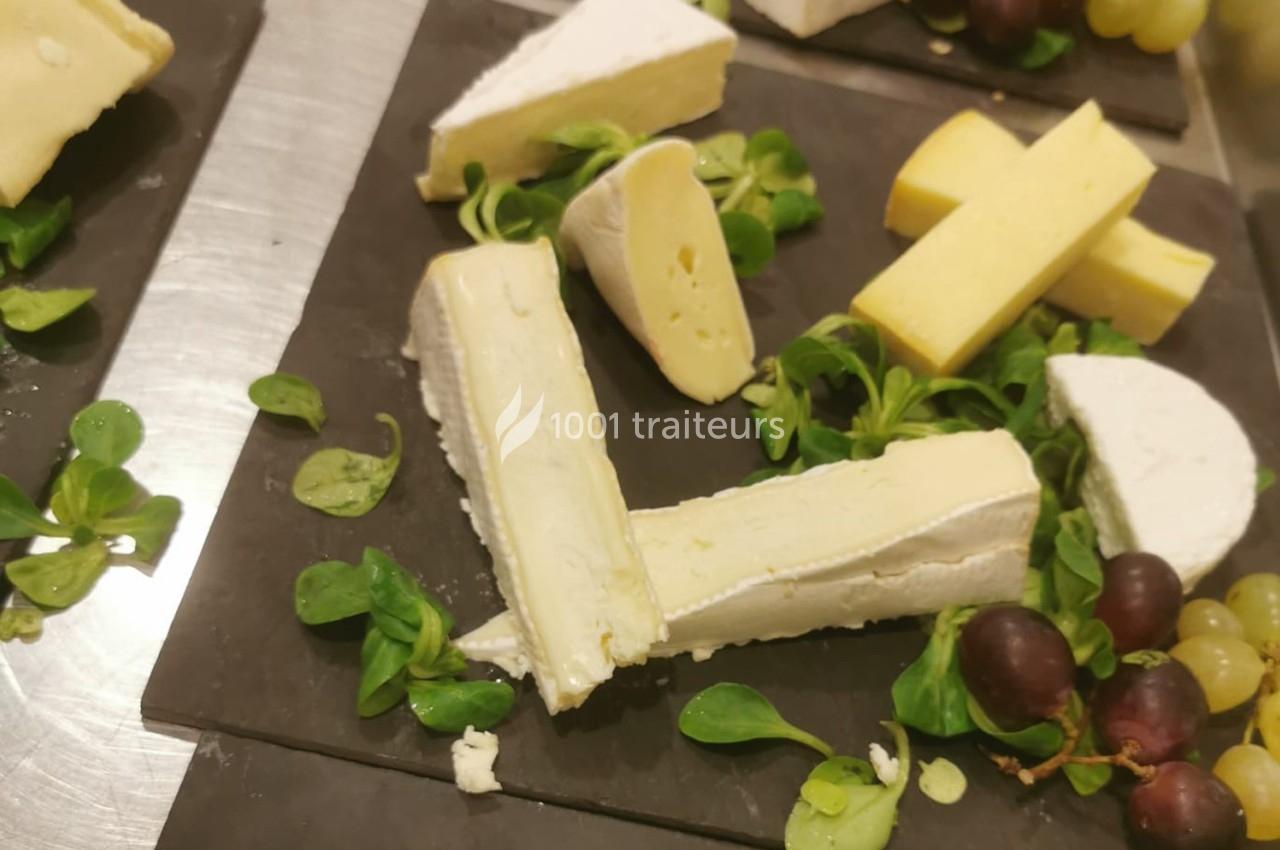 Assortiment de fromages sur une ardoise avec mâche, raisins rouges et verts.