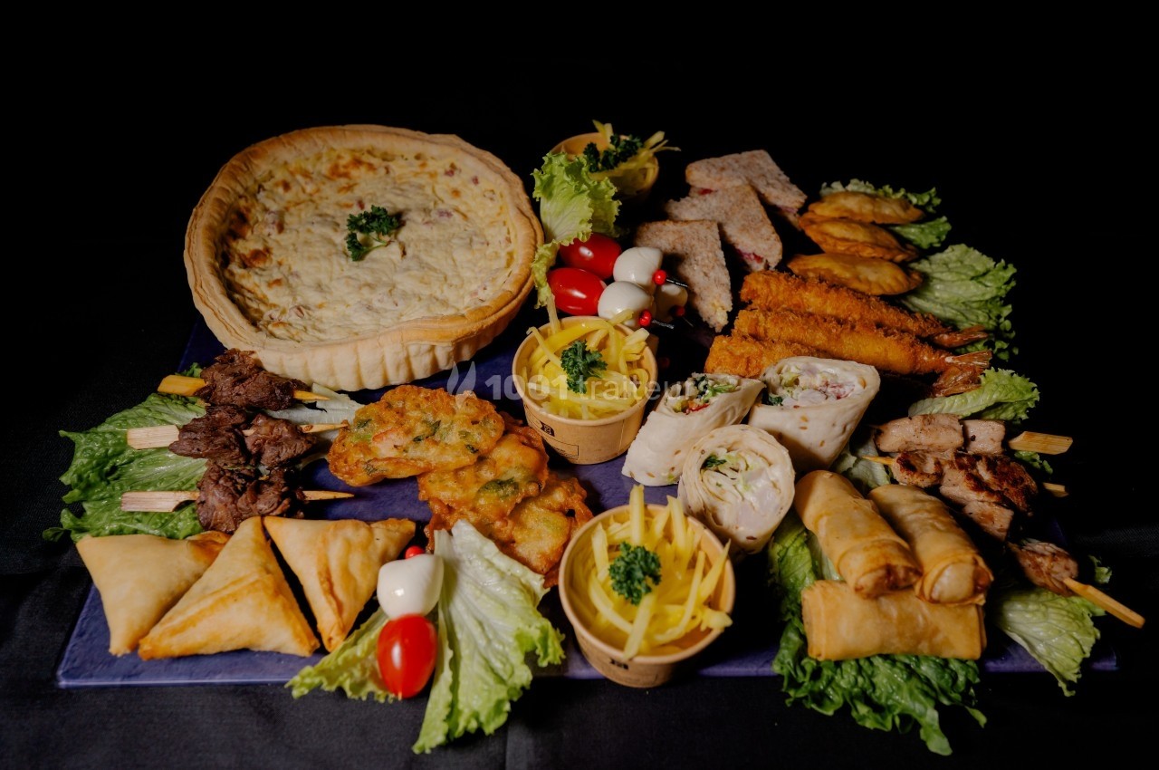 Plateau de mets variés comprenant quiche, brochettes, rouleaux, feuilletés et légumes sur lit de salade.