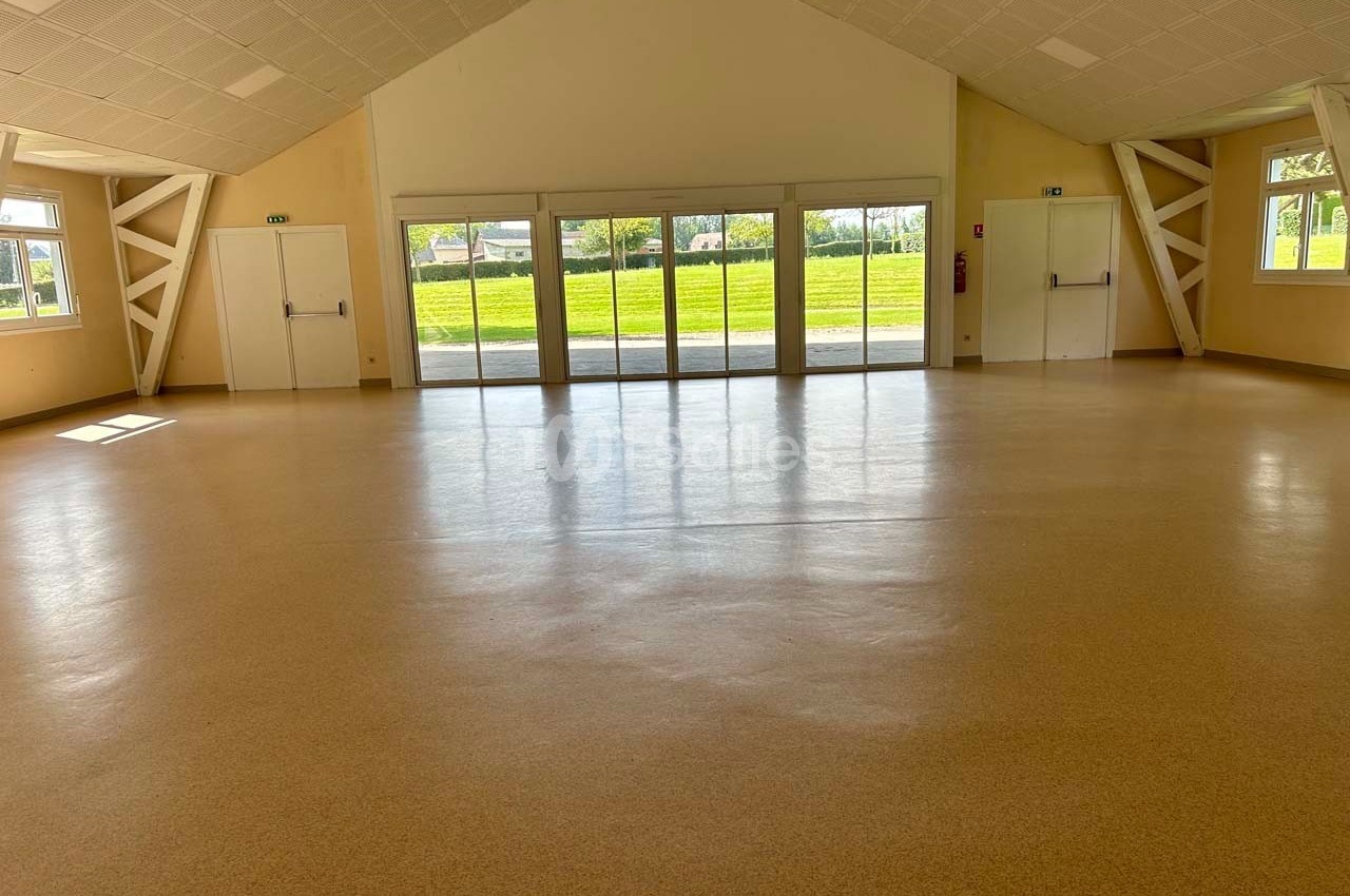 Salle vide avec sol en linoléum clair, grandes fenêtres laissant entrer la lumière naturelle et plafond incliné.
