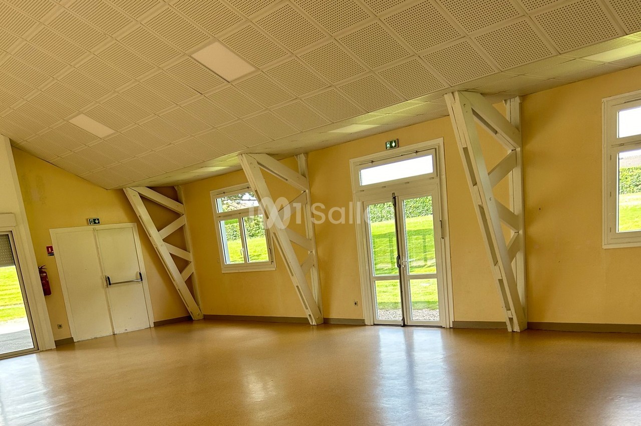 Salle lumineuse avec murs jaunes, plafond incliné, fenêtres et porte vitrée donnant sur un espace extérieur verdoyant.