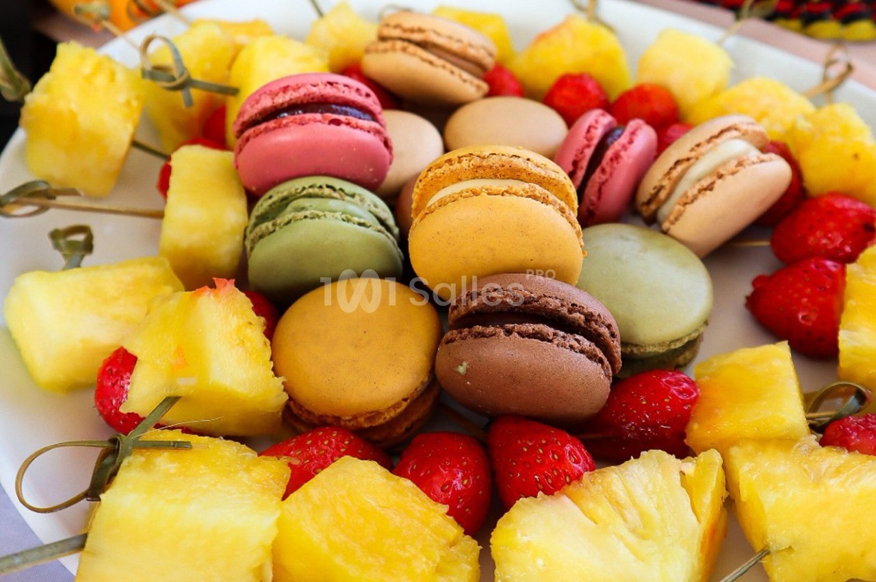 Assortiment de macarons colorés entourés de morceaux d'ananas et de fraises sur un plateau.