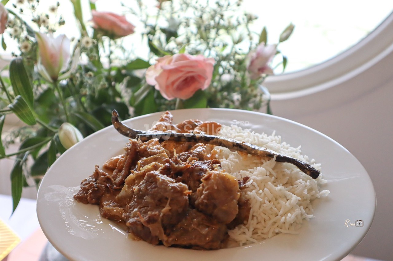 Assiette de riz blanc accompagné d'un plat en sauce avec une gousse de vanille, posée devant un bouquet de fleurs.