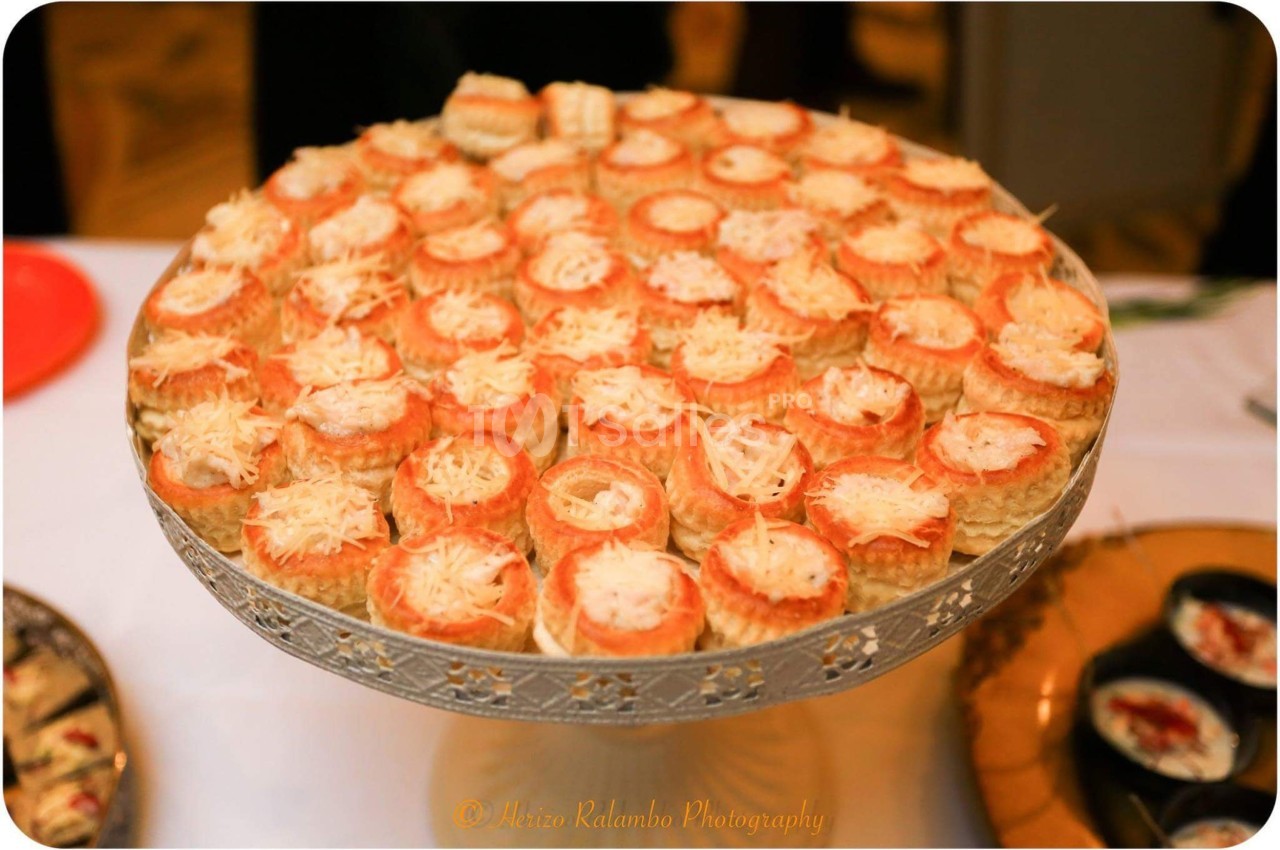 Plateau de bouchées feuilletées garnies de fromage râpé, présenté sur un support décoratif en métal argenté.