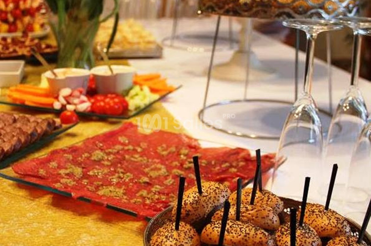 Table dressée avec des amuse-bouches, mini-sandwichs au sésame, légumes, fromages et décorations florales.