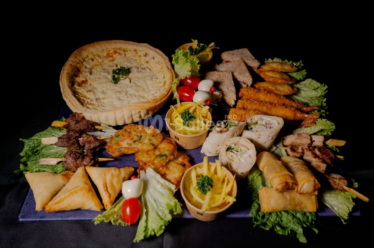 Plateau varié de mets salés comprenant quiche, brochettes, samoussas, rouleaux de printemps et autres amuse-bouches.