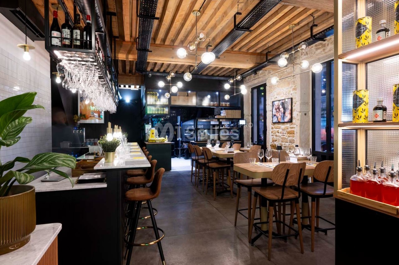 Intérieur d'un restaurant moderne avec bar, tables en bois, éclairage suspendu et murs en pierre apparente.