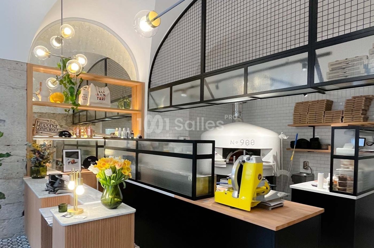 Intérieur d'une pizzeria moderne avec un four à bois, un comptoir en bois et des décorations florales.