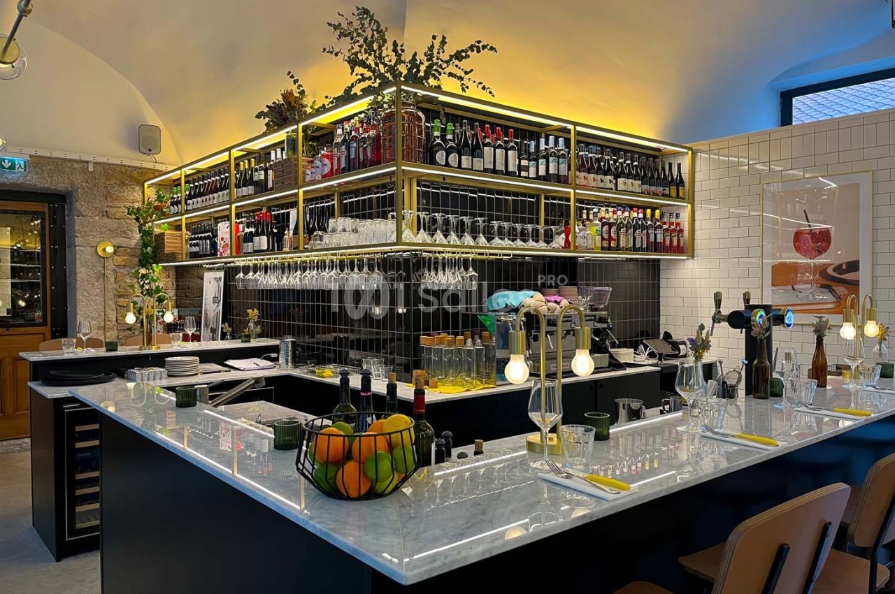 Bar moderne avec comptoir en marbre, étagères garnies de bouteilles et ambiance chaleureuse éclairée.
