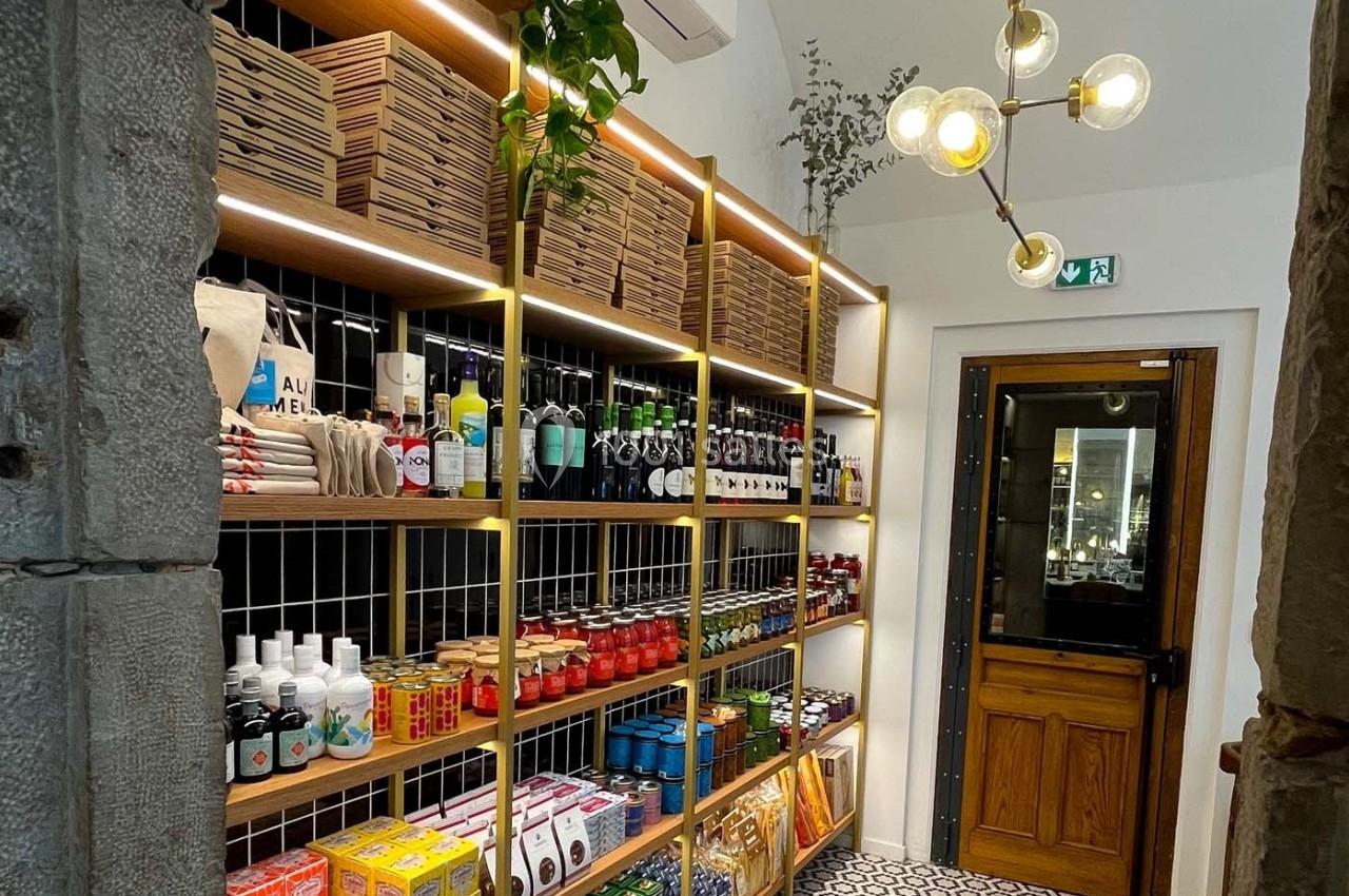 Étagères en bois remplies de produits alimentaires et bouteilles, éclairées par des lumières suspendues dans une boutique.