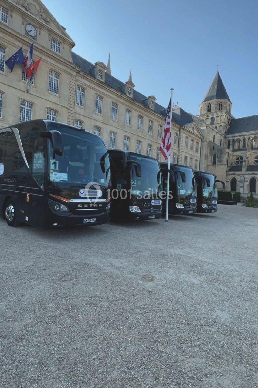 Cinq autocars noirs stationnés devant un bâtiment historique avec drapeaux français et américain visibles.