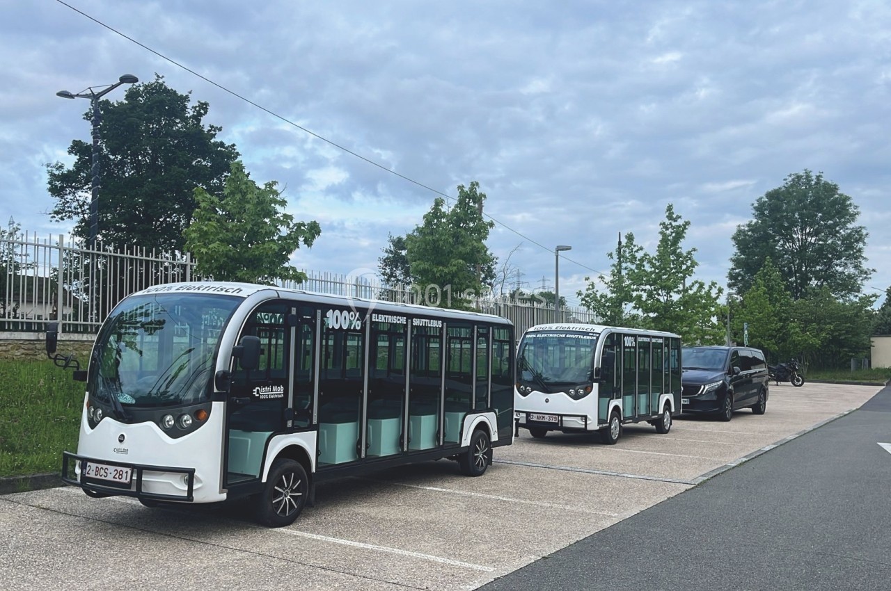 Deux minibus électriques stationnés sur un parking, entourés d'arbres et de bâtiments résidentiels.