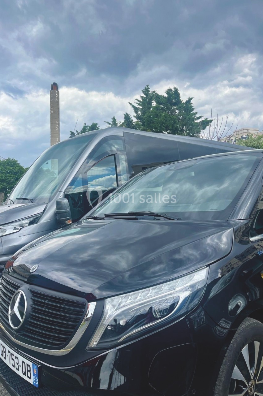 Deux véhicules Mercedes noirs stationnés sur un parking, avec un ciel nuageux en arrière-plan.