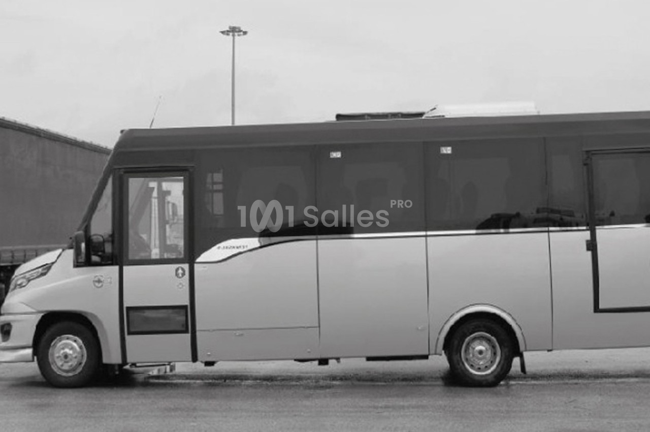 Minibus stationné sur une surface pavée, vu de profil, avec un bâtiment industriel en arrière-plan.