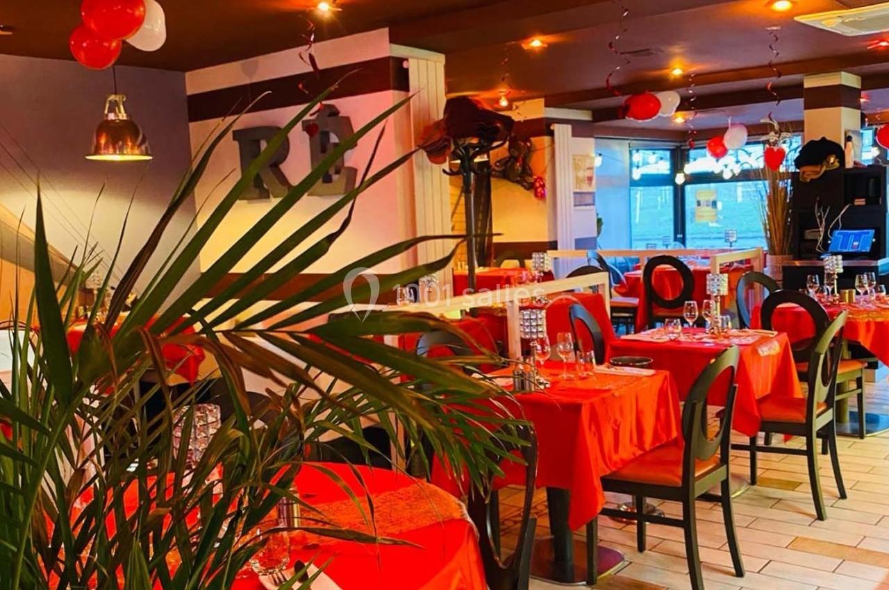 Salle de restaurant décorée avec des nappes rouges, des ballons et une lumière chaleureuse.