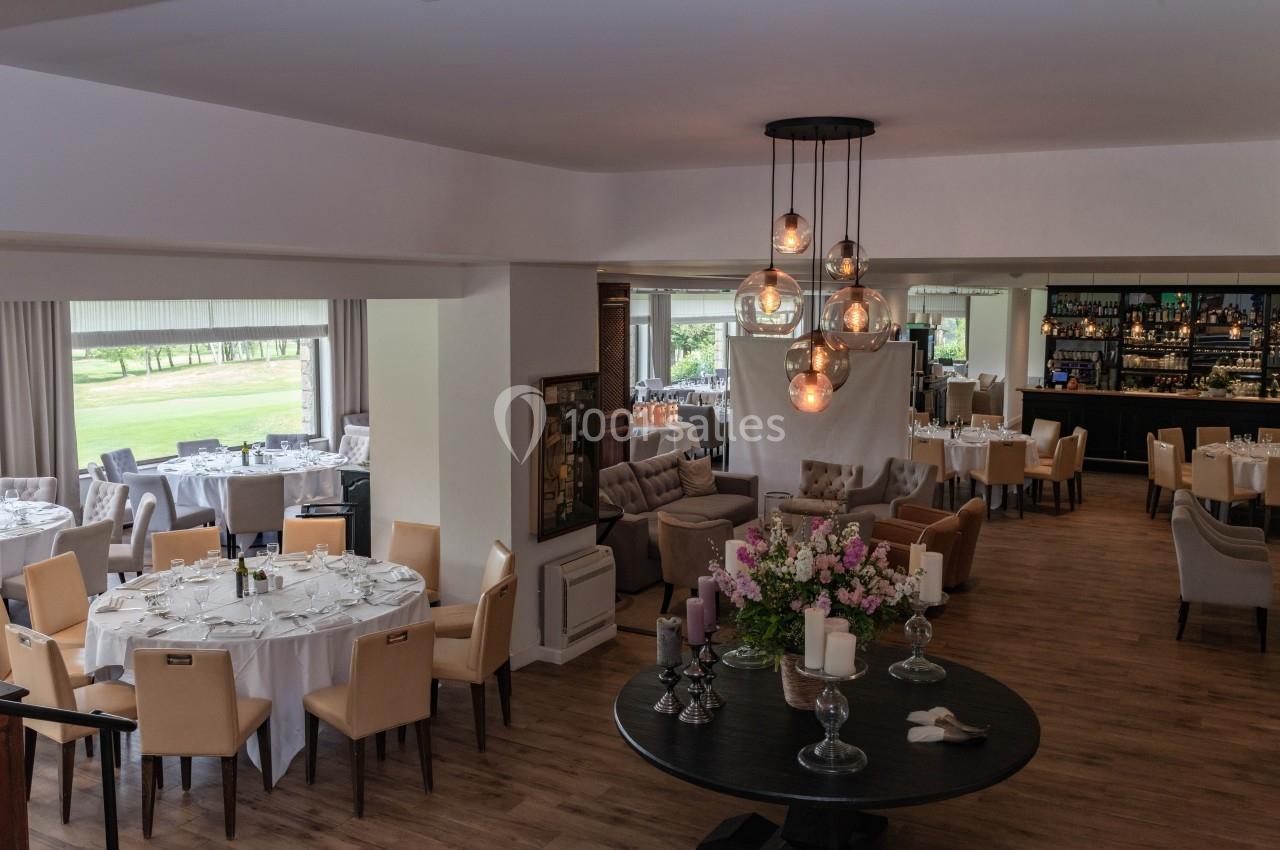Salle de restaurant élégante avec tables dressées, grandes baies vitrées et un bar en arrière-plan.