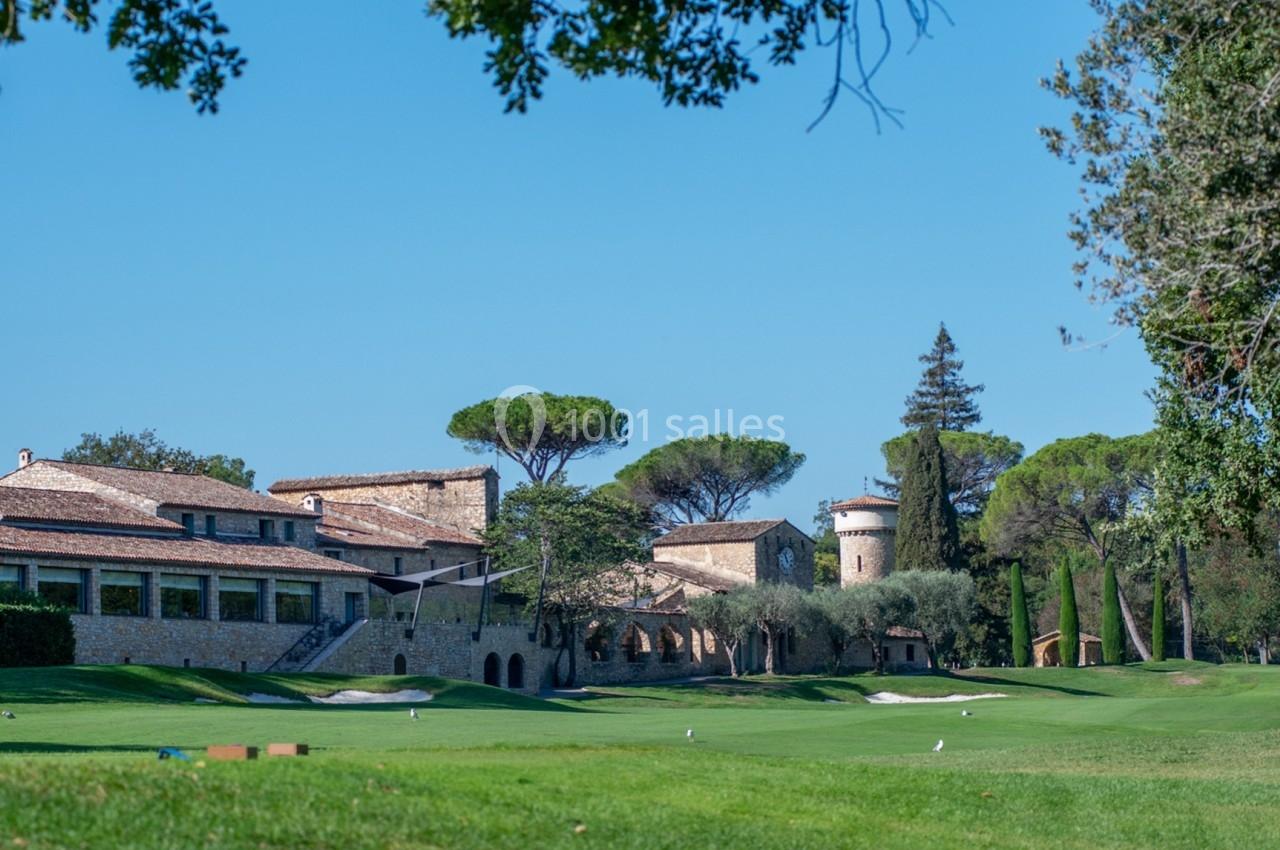 Vue d'un bâtiment en pierre entouré d'arbres et d'un terrain de golf sous un ciel dégagé.