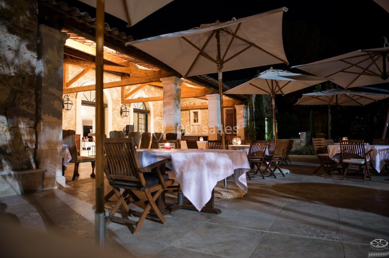 Terrasse d'un restaurant éclairée de nuit, avec des tables dressées, des chaises en bois et des parasols ouverts.