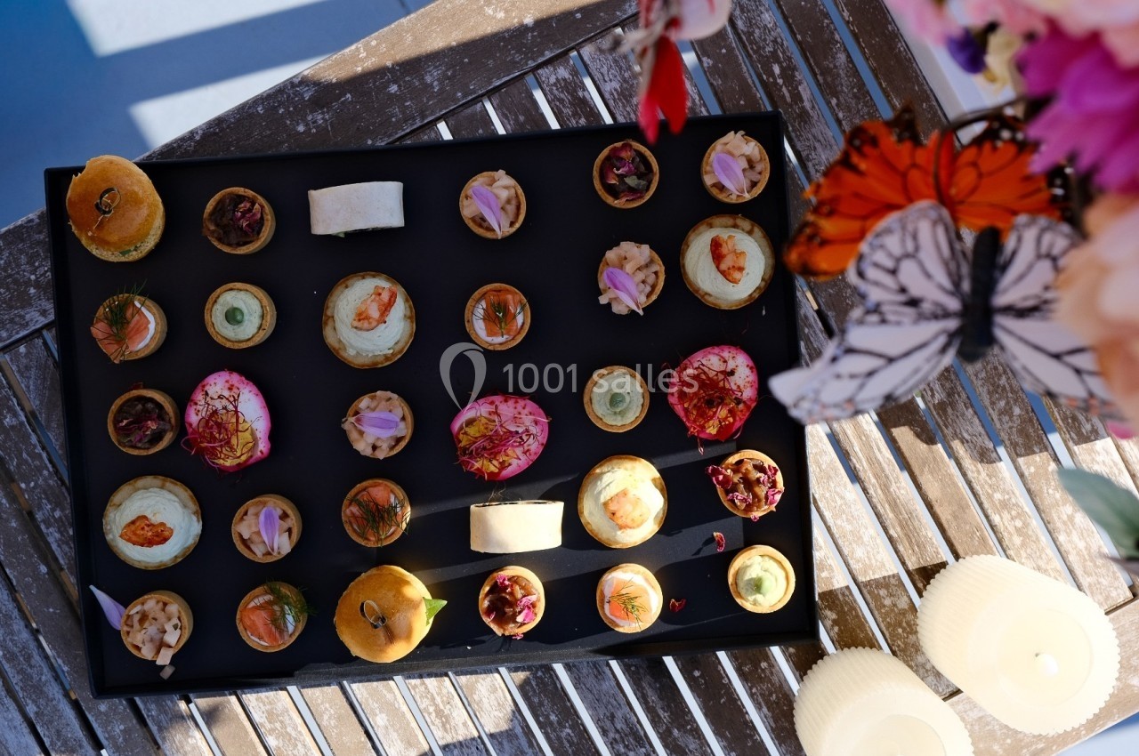 Plateau de canapés variés disposés sur une table en bois, décorée de fleurs et de bougies.