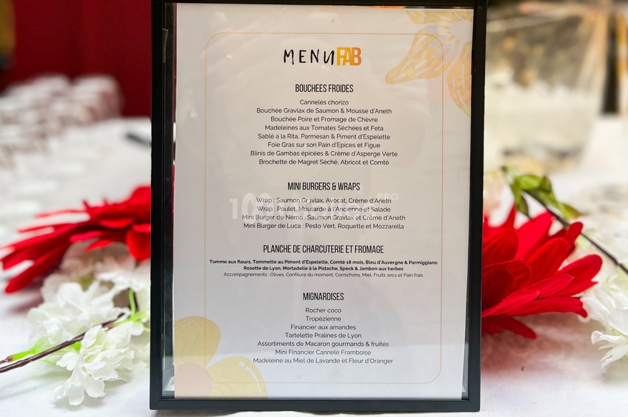 Carte de menu encadrée posée sur une table, entourée de fleurs rouges et blanches.