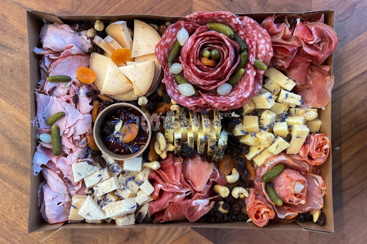 Plateau garni de charcuteries, fromages variés, fruits secs, cornichons et confiture, présenté sur une table en bois.