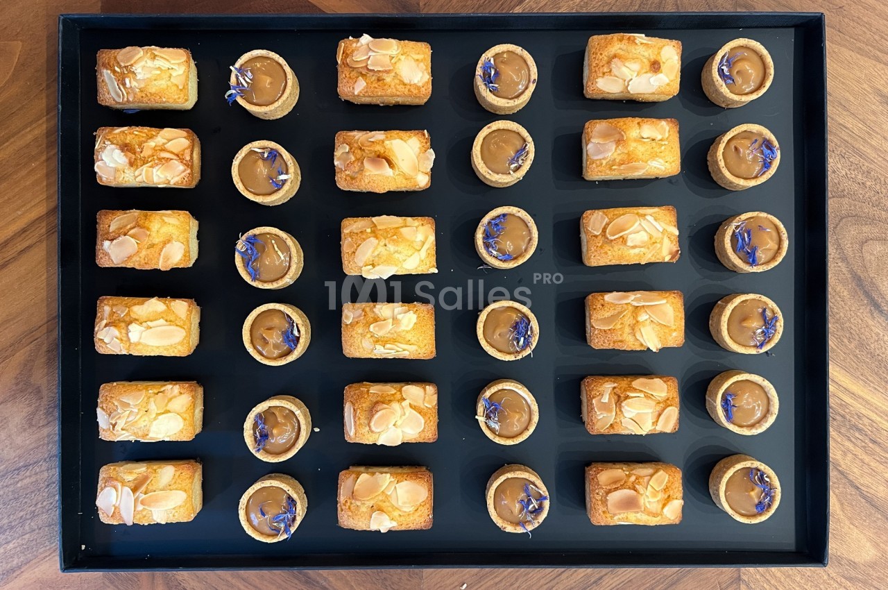 Plateau de mignardises composé de financiers aux amandes et de tartelettes au caramel décorées de fleurs bleues.