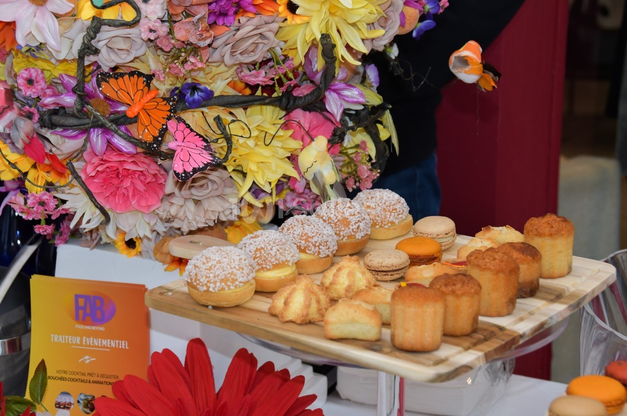 Plateau de pâtisseries variées disposé devant une décoration florale colorée avec des papillons.