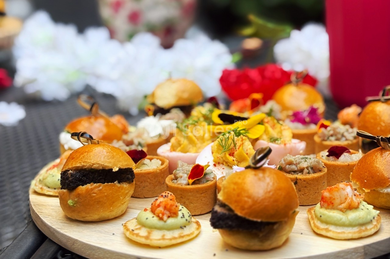 Plateau de bouchées apéritives variées avec mini-burgers, tartelettes et canapés, décoré de fleurs comestibles.
