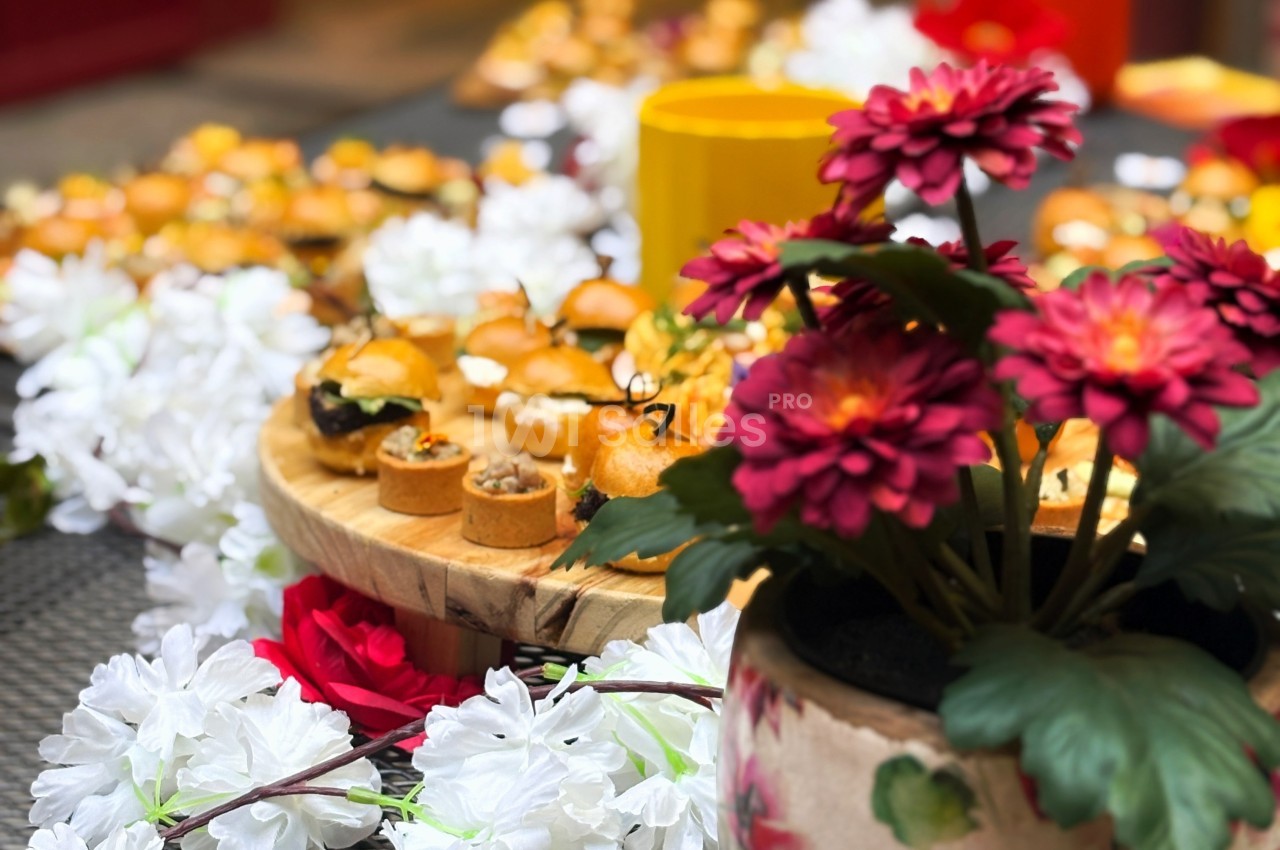 Plateau de bouchées apéritives sur une table décorée de fleurs blanches et rouges, avec un pot de fleurs au premier plan.
