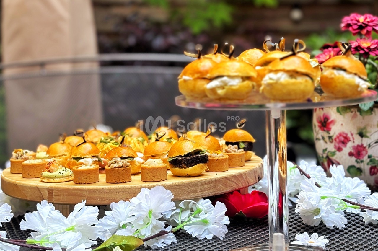 Plateau de mini-burgers et bouchées salées disposé sur une table décorée de fleurs blanches et rouges.