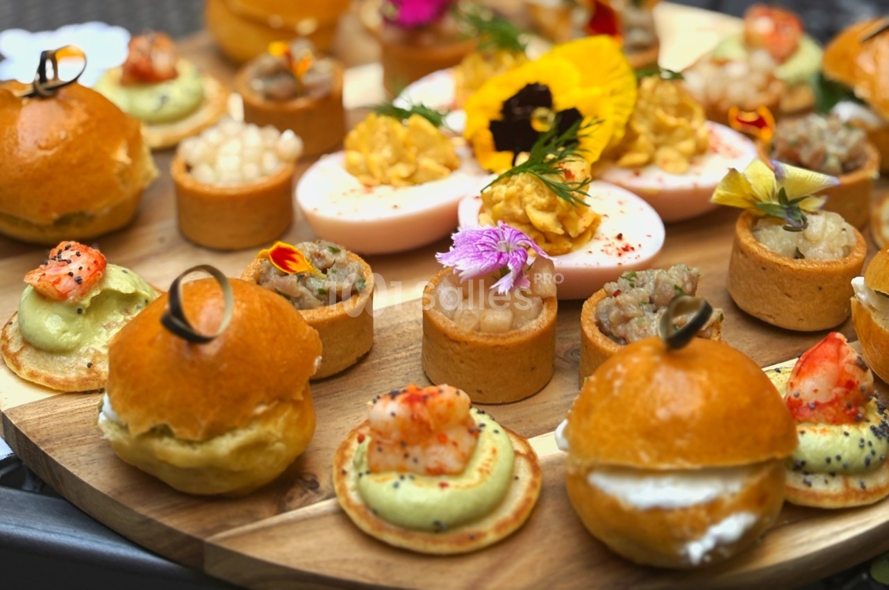 Plateau de bouchées apéritives variées avec mini-burgers, tartelettes, œufs farcis et décorations florales.