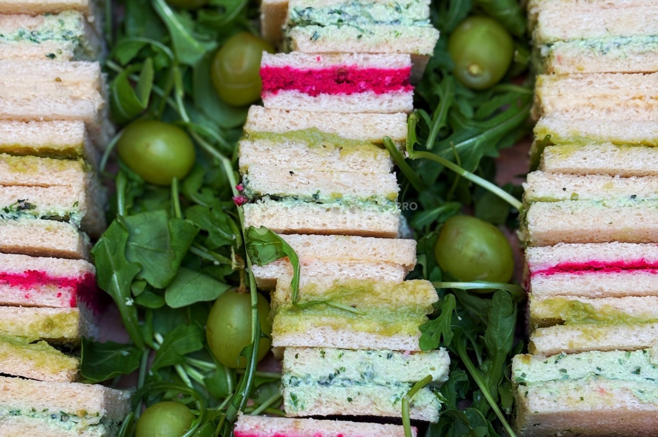 Sandwiches colorés empilés avec des garnitures variées, entourés de roquette et d'olives vertes.
