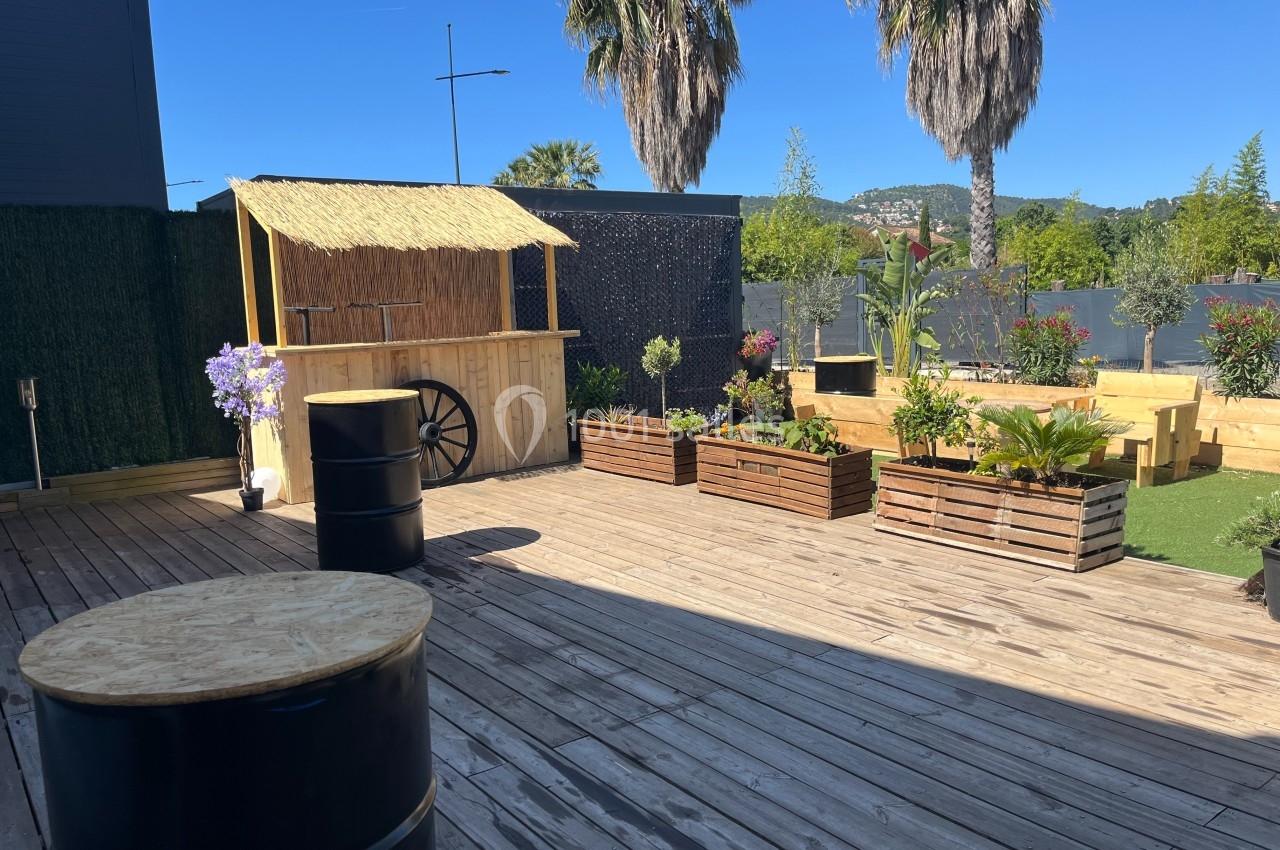 Terrasse en bois avec des jardinières, un bar en bois au toit de chaume et des palmiers en arrière-plan.