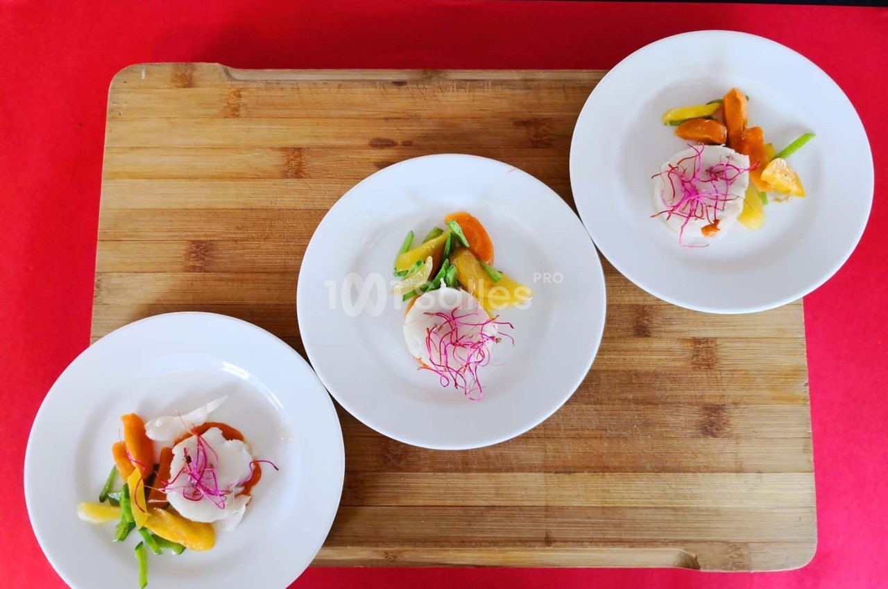 Trois assiettes blanches contenant des légumes colorés et une garniture de pousses roses, disposées sur une planche en bois.