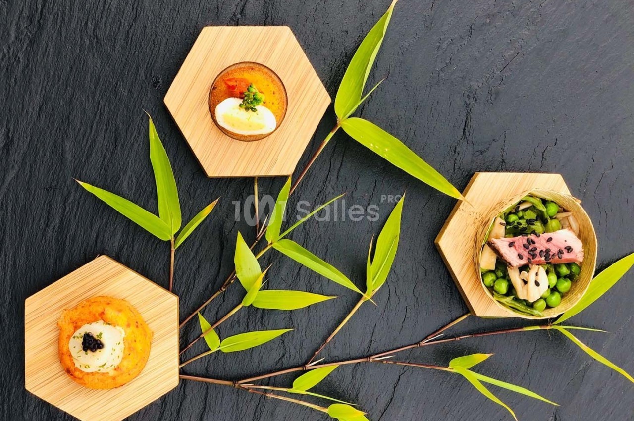 Assortiment de plats gastronomiques présentés sur des assiettes hexagonales en bois, décorés de feuilles de bambou.