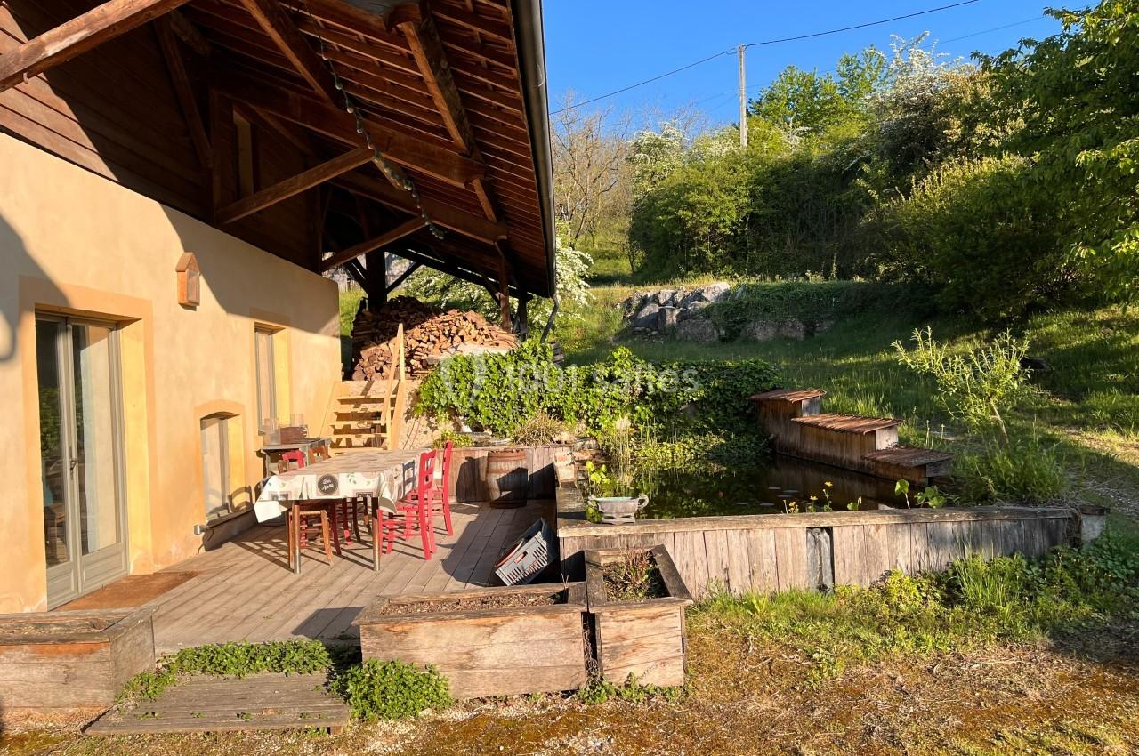 Terrasse en bois avec table et chaises rouges, bordée de jardinières, située près d'une maison et entourée de verdure.