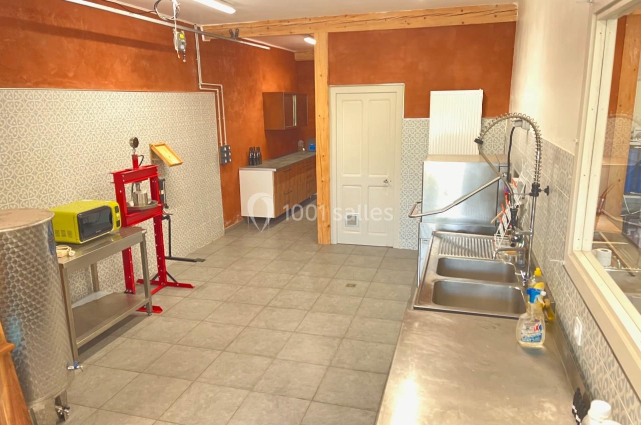 Atelier équipé avec évier, presse, cuves en inox et mobilier, murs carrelés et peints en orange.