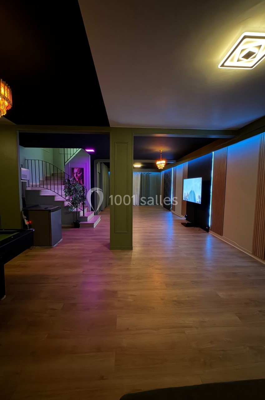 Salle moderne avec parquet, éclairage tamisé, télévision, billard et escalier en arrière-plan.